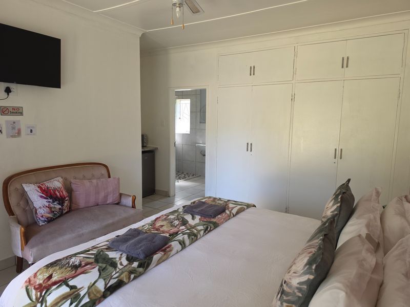 A bedroom featuring built-in cupboards, a ceiling fan, and an adjoining bathroom, offering a functional and comfortable layout for guests.