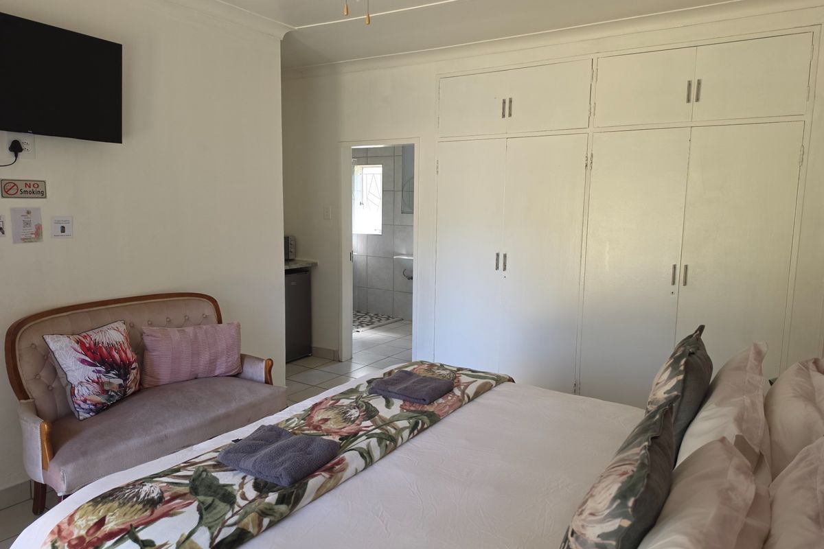 A bedroom featuring built-in cupboards, a ceiling fan, and an adjoining bathroom, offering a functional and comfortable layout for guests.