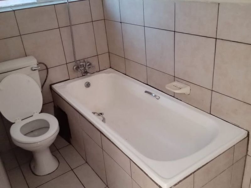 A functional bathroom featuring a built-in bathtub, toilet, and tiled finishes, requiring cosmetic updates to improve its overall aesthetic appeal.