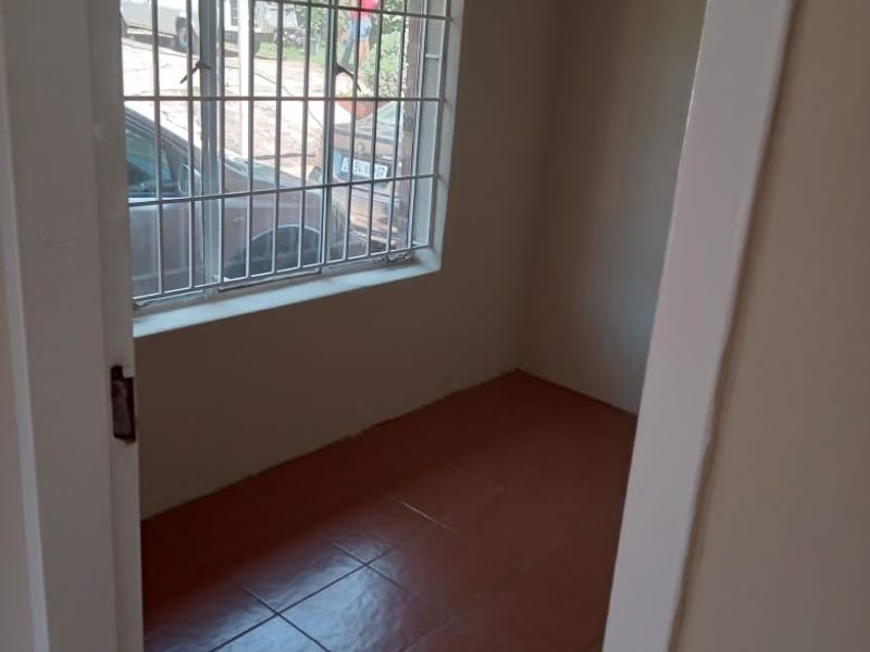 A compact, empty bedroom featuring tiled flooring and a window fitted with security bars.