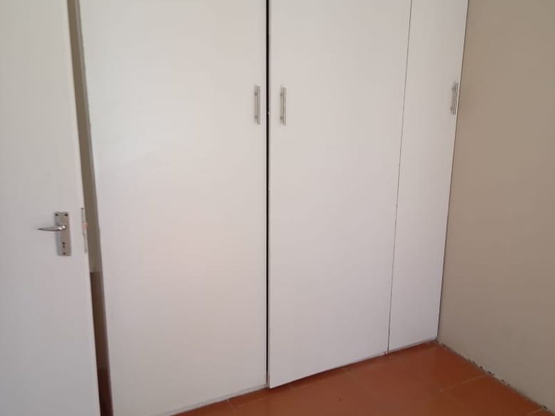 A simple bedroom featuring built-in white wardrobes and terracotta-style floor tiles, offering a clean and functional space ready for personalization.