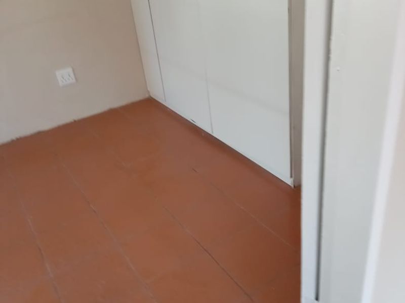 A vacant bedroom featuring built-in wardrobes and terracotta-style tiled flooring, requiring minor cosmetic updates to improve the overall finish.