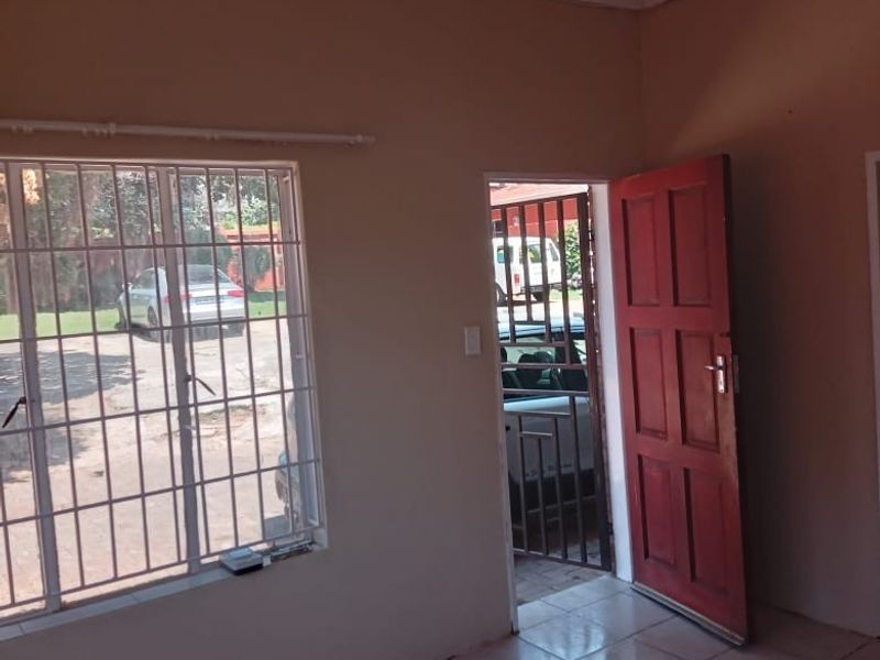 An empty living room featuring tiled flooring, security bars on the windows, and a timber entrance door leading to the exterior.
