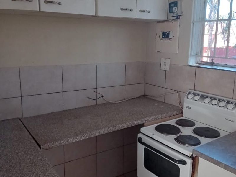 A functional kitchen featuring built-in cabinetry, stone-look countertops, ceramic tiling, and a freestanding electric stove, with security bars on the window.