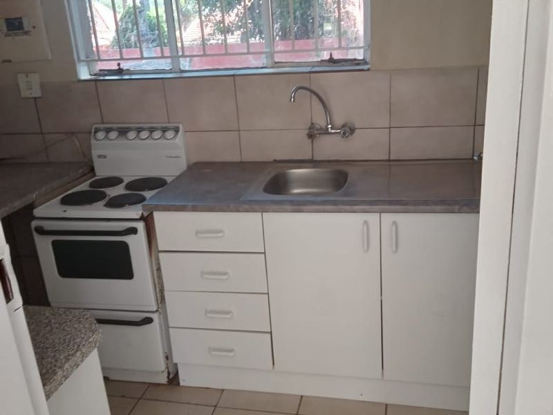 A compact, functional kitchen featuring white cabinetry, a built-in stove, stainless steel sink, and tiled flooring, offering a clean space ready for updates.