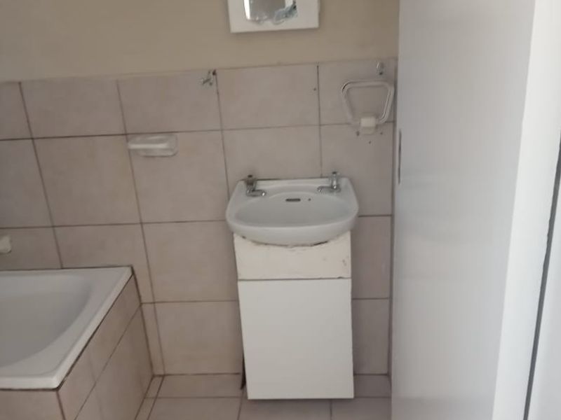 A functional bathroom featuring a built-in bathtub, wall-mounted basin with vanity cabinet, and neutral wall and floor tiling.
