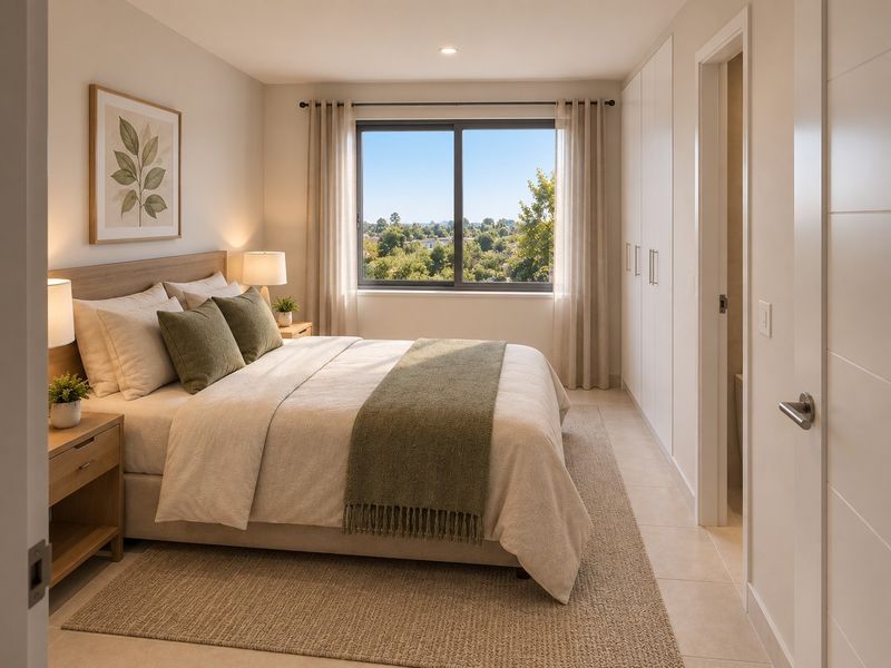 A bright and modern bedroom featuring built-in cupboards, neutral tiled flooring, and a large window offering pleasant outdoor views.