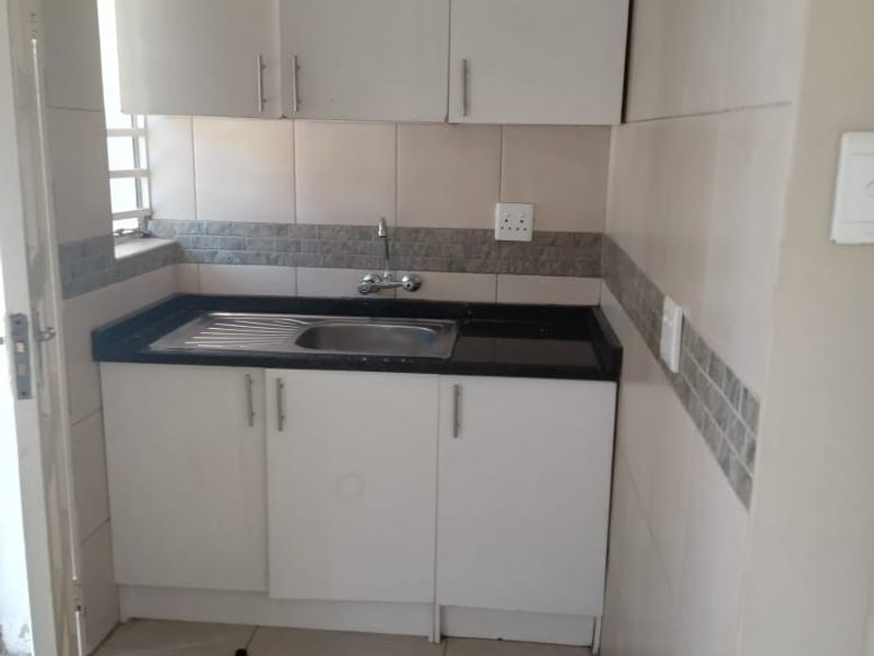 A compact scullery or utility area featuring white built-in cabinetry, a stainless steel sink, and neutral tiled finishes throughout.