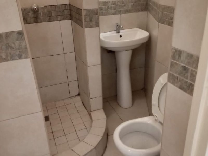 Compact bathroom featuring a tiled shower enclosure, pedestal washbasin, and toilet with neutral ceramic wall and floor tiling.