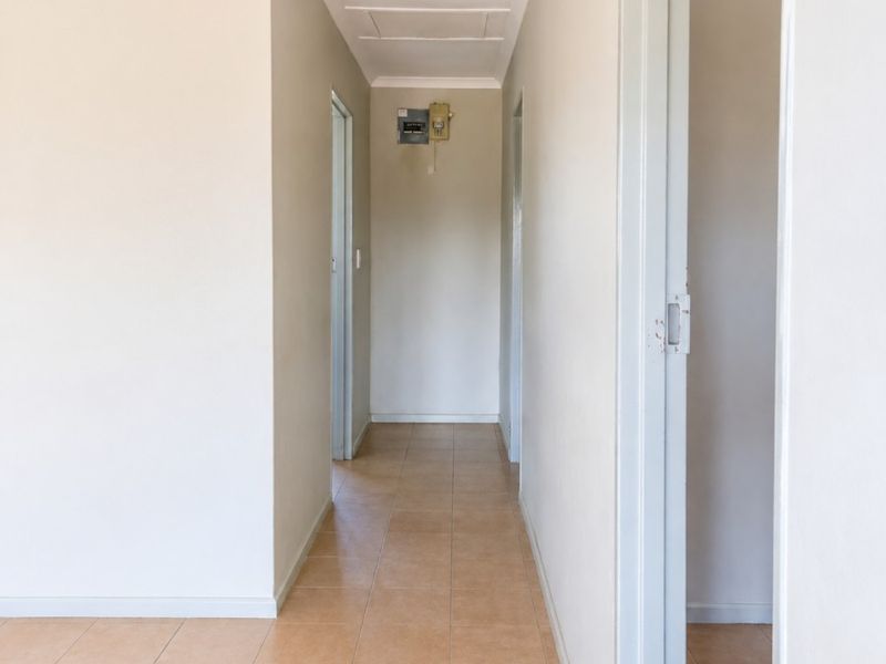 A clean, empty hallway featuring neutral wall tones, ceramic floor tiles, and a ceiling access hatch, providing access to multiple rooms.