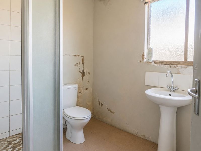 A bathroom featuring a shower enclosure, pedestal basin, and toilet, currently requiring significant wall repairs and cosmetic updates to restore its condition.