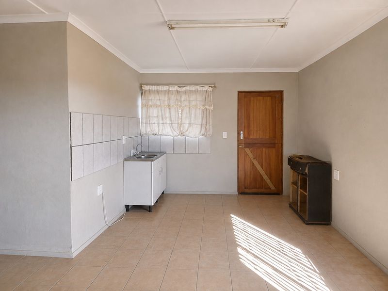 A compact, empty kitchen area featuring tiled flooring, a single basin sink with tiled splashback, and a wooden exterior door.