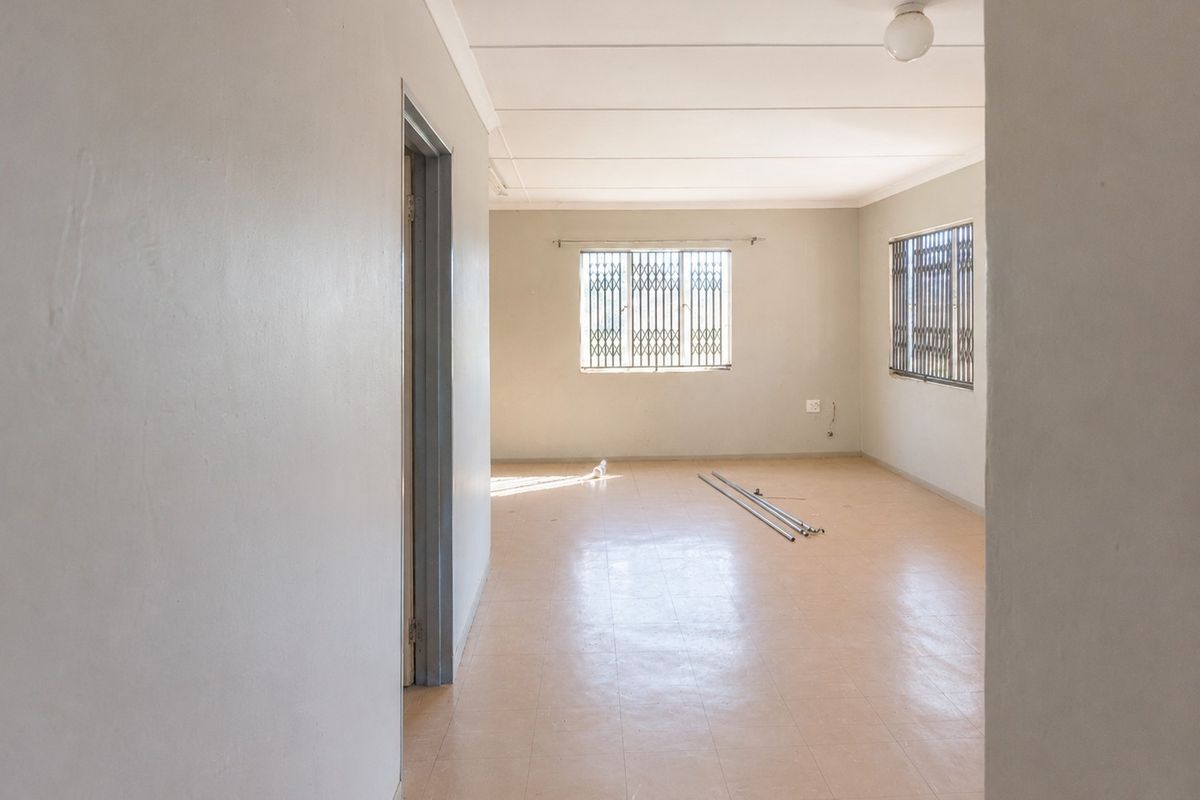 A spacious, empty living area featuring neutral walls, tiled flooring, and security gates on the windows, offering a blank canvas for interior design.
