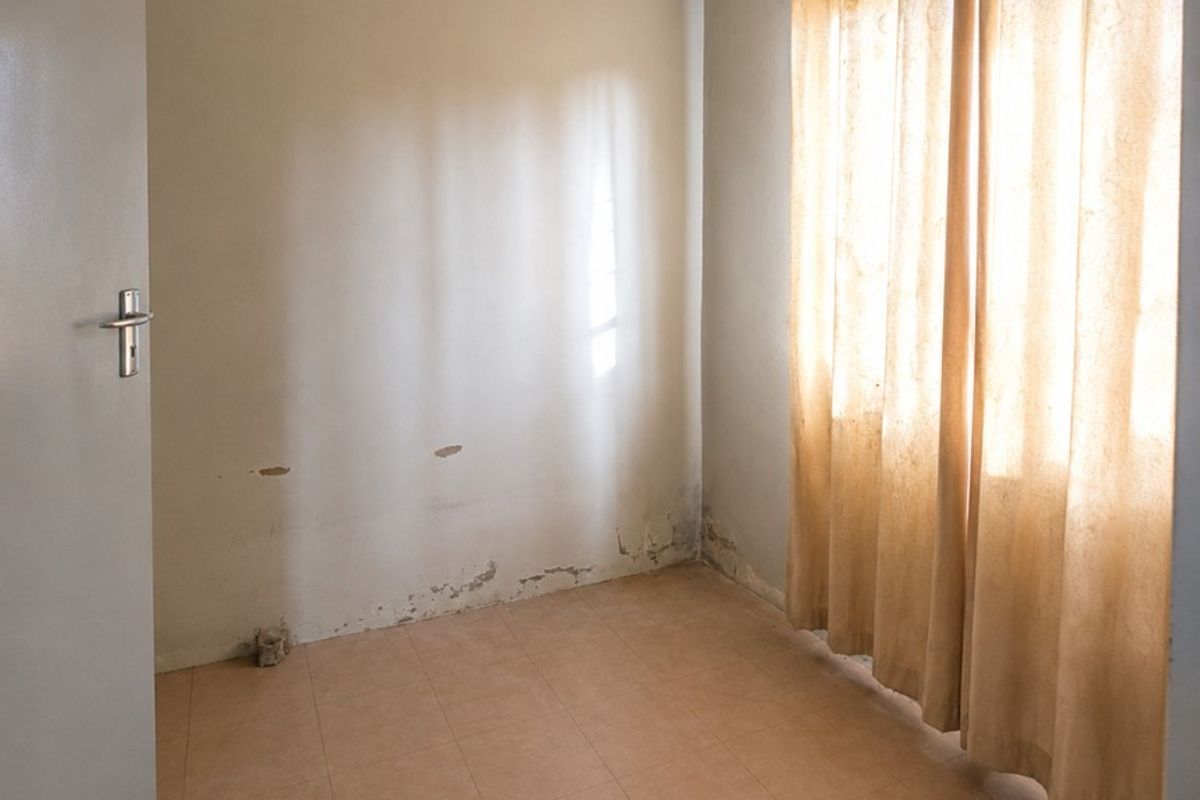 An empty bedroom featuring tiled flooring and cove cornicing, currently showing signs of wall surface deterioration and dampness requiring maintenance.