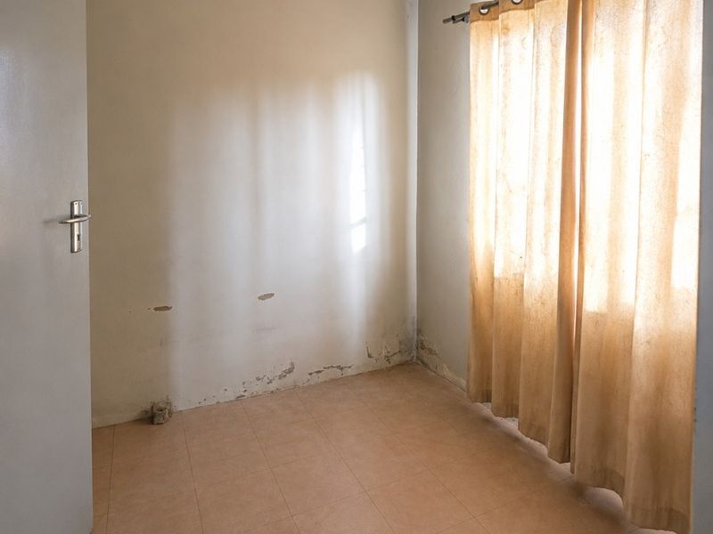 An empty bedroom featuring tiled flooring and cove cornicing, currently showing signs of wall surface deterioration and dampness requiring maintenance.
