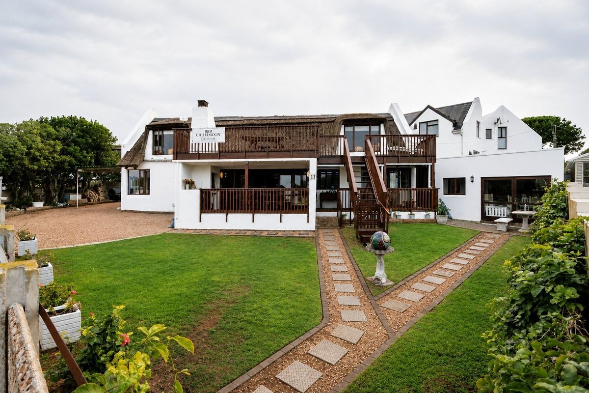 Rear view of a two-story house featuring a thatched roof, a large timber balcony with an external staircase, and a well-maintained garden with paved pathways.