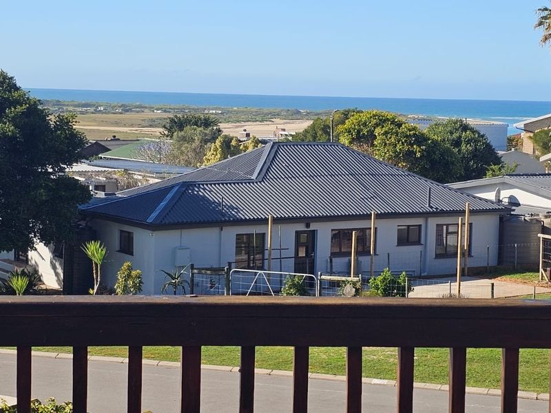 Elevated view overlooking a residential property with a metal roof, coastal landscape, and ocean horizon in the background.