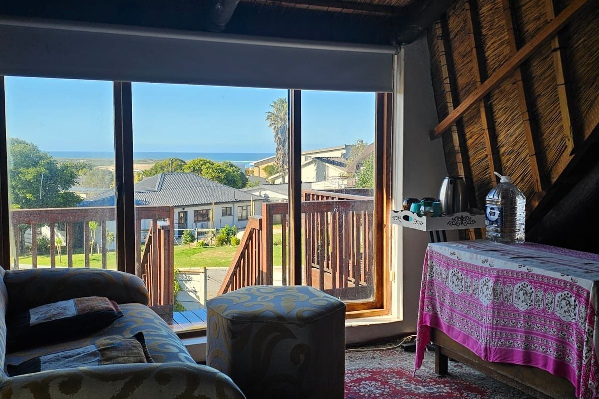 Living area featuring exposed thatch roof rafters and large sliding doors opening onto a wooden deck with coastal views.