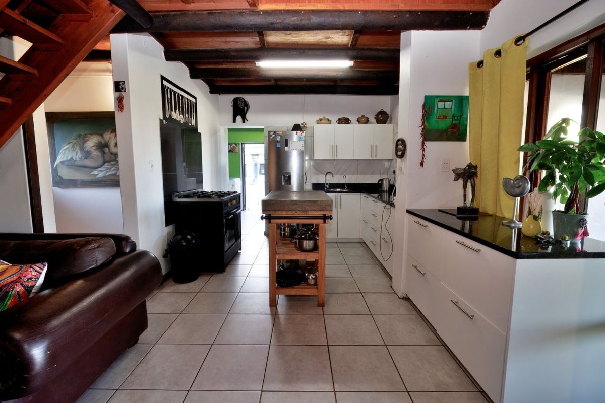 A functional kitchen featuring white cabinetry, granite countertops, a central island, and exposed timber ceiling beams, with tiled flooring throughout.