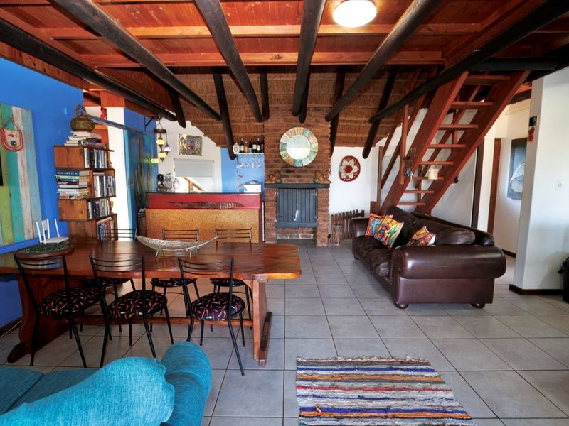 Spacious open-plan living and dining area featuring exposed timber ceiling beams, a brick fireplace, and a built-in bar, with an integrated timber staircase.