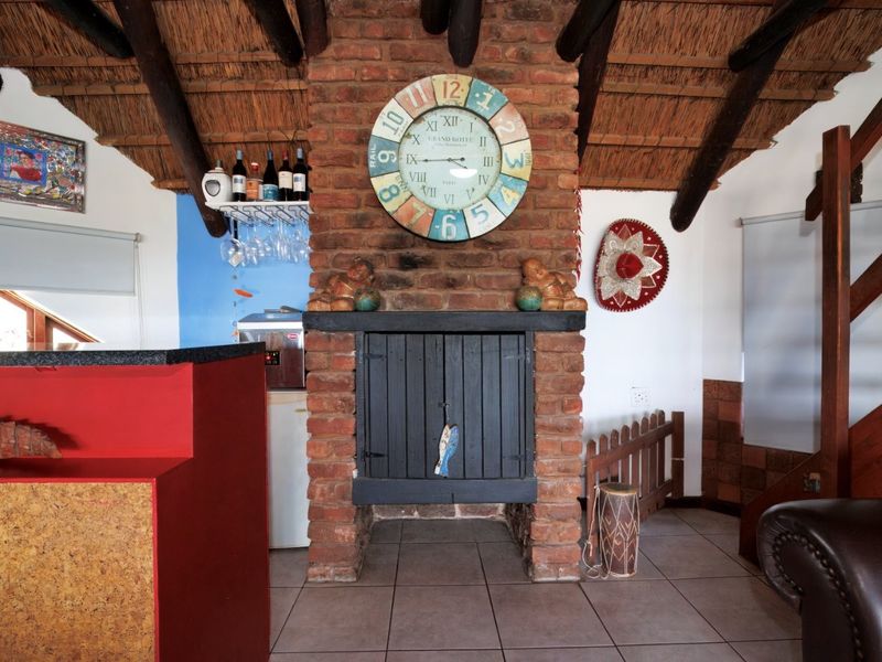 A rustic bar area featuring an exposed brick fireplace, thatched roof with timber beams, and a built-in bar counter with tiled flooring.