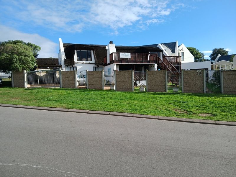 Front elevation of a two-story house featuring a thatched roof, a prominent timber balcony with external stairs, and a secure precast concrete boundary wall.