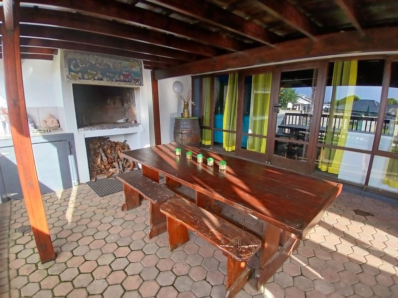 Covered outdoor patio featuring a built-in braai, timber pergola structure, and paved flooring, providing a functional space for outdoor entertaining.