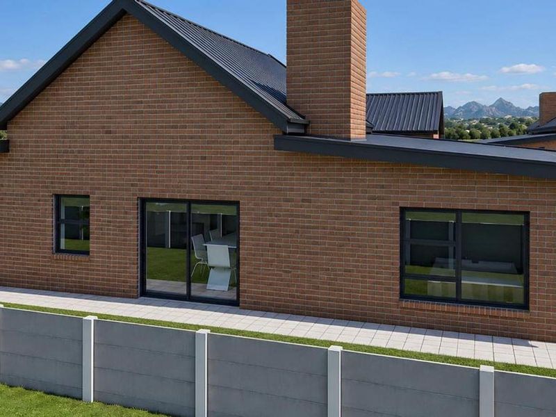 Rear view of a modern brick house featuring a metal roof, chimney, paved patio area, and secure perimeter walling with scenic mountain views.