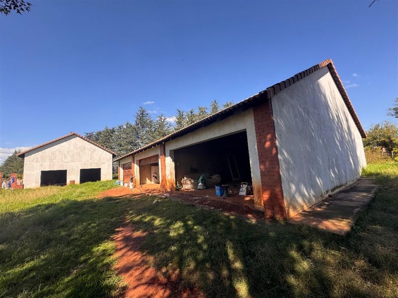 Rear view of an unfinished outbuilding or garage structure featuring brick masonry and tiled roofing, set on an undeveloped plot of land.