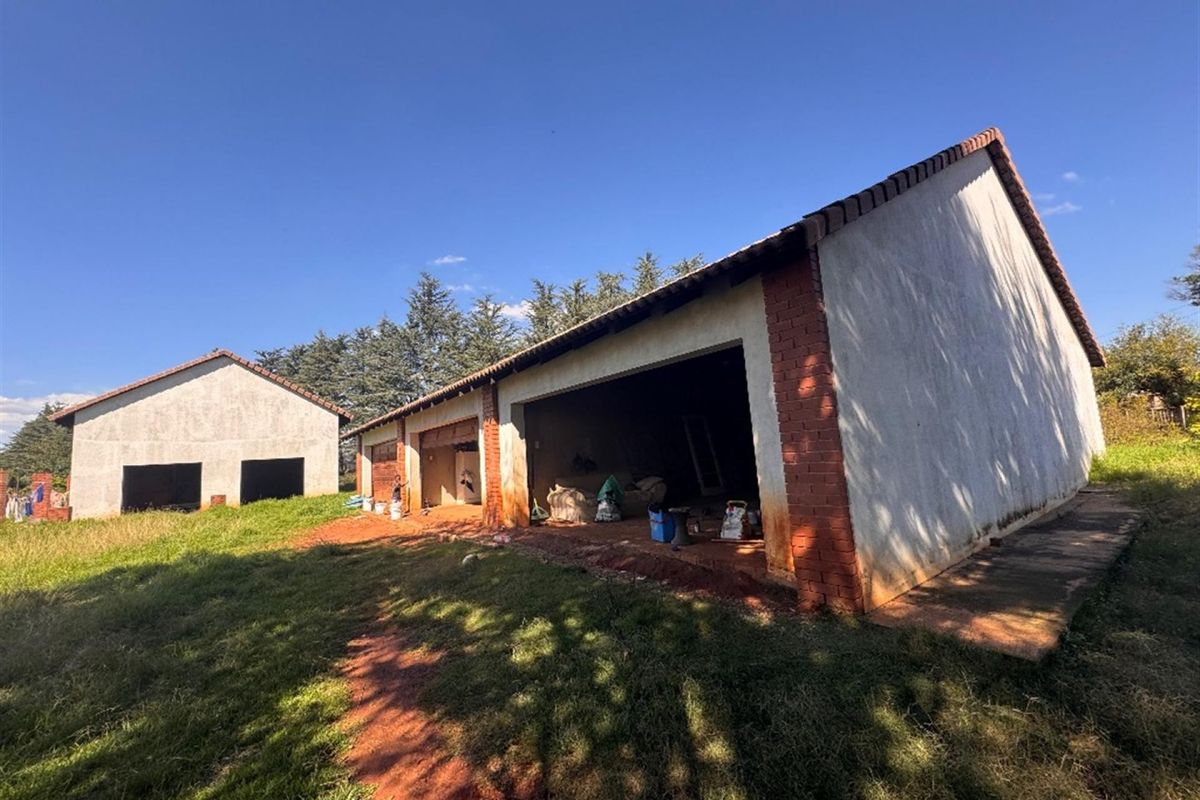 Rear view of an unfinished outbuilding or garage structure featuring brick masonry and tiled roofing, set on an undeveloped plot of land.