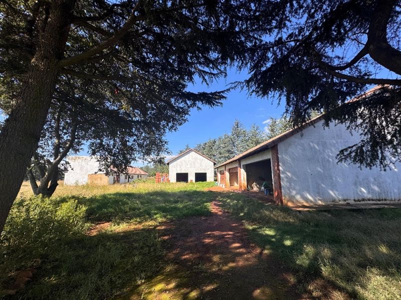 View of multiple outbuildings on a large plot, featuring traditional brick and plaster construction with tiled roofs, surrounded by mature trees and overgrown grounds.