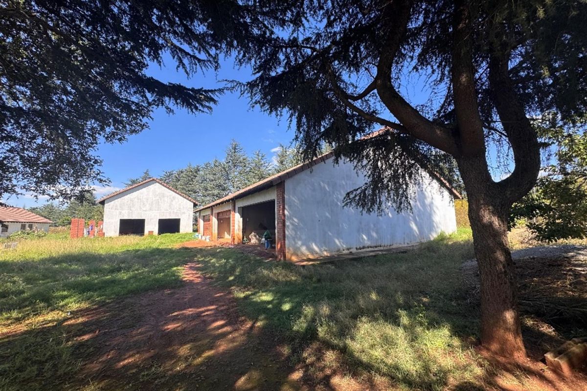 Exterior view of detached outbuildings or garage structures featuring unfinished masonry walls and pitched roofs set within a large, overgrown garden area.