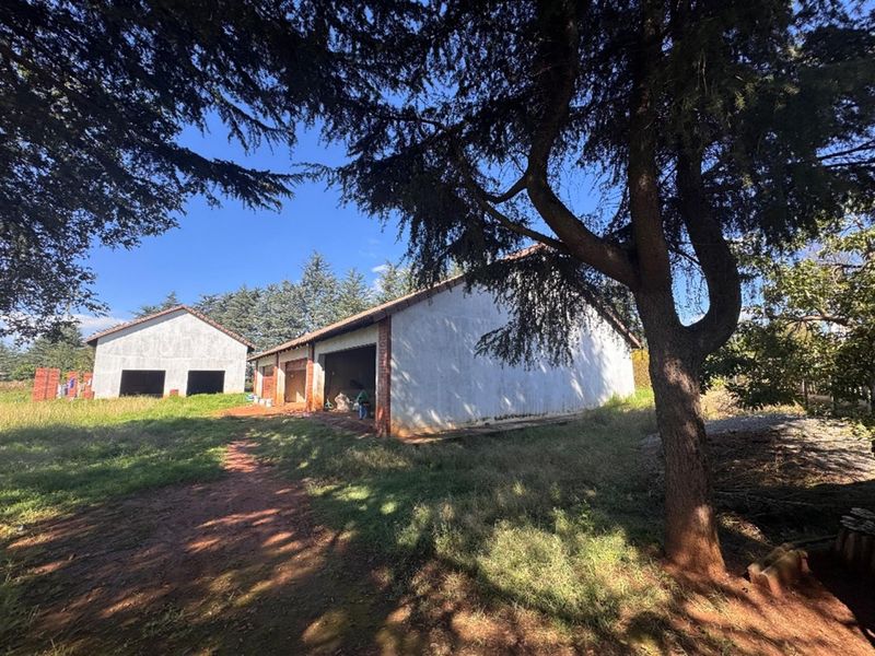Exterior view of unfinished outbuildings or garage structures featuring brick construction and tiled roofing set within a large garden area.