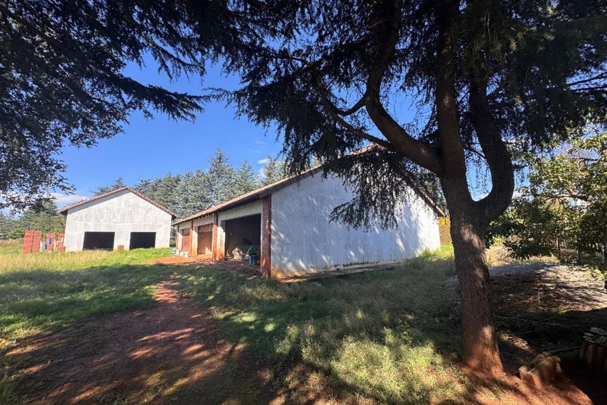Exterior view of unfinished outbuildings or garage structures featuring brick construction and tiled roofing set within a large garden area.