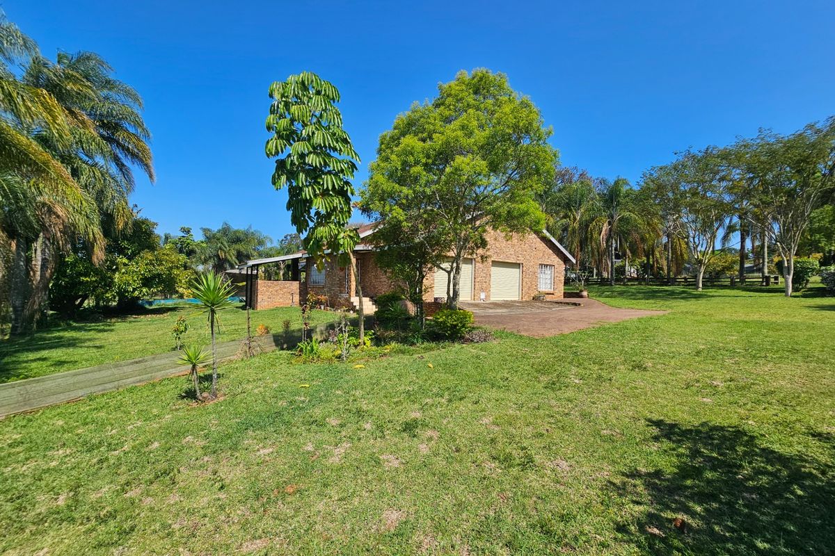 A view of the rear brick facade of the house featuring a double garage, paved driveway, and expansive surrounding garden.