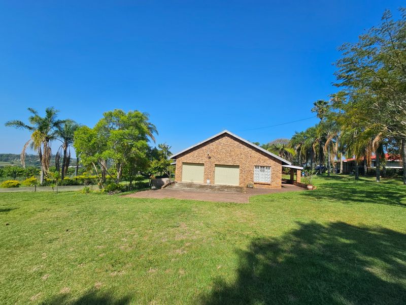 A detached brick double garage set within a spacious, well-maintained garden with mature trees and a paved driveway.
