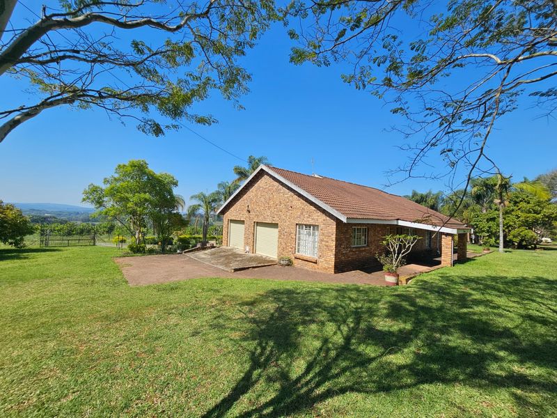 A rear view of a face brick house featuring a double garage, covered patio, and expansive surrounding garden area.