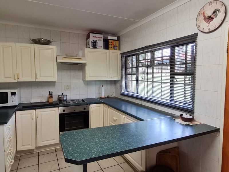 Functional kitchen featuring built-in cabinetry, laminate countertops, integrated oven and hob, tiled backsplash, and tiled flooring with a breakfast nook area.