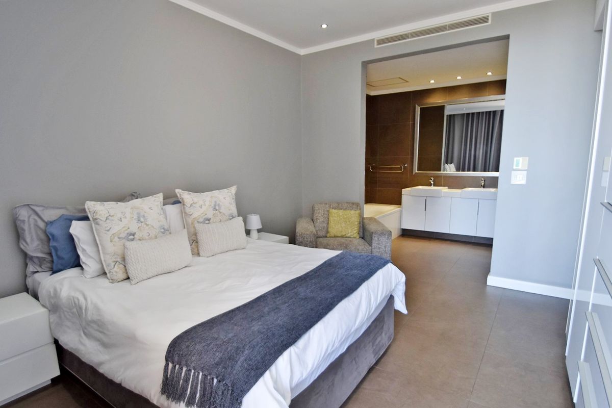 Spacious bedroom featuring an open-plan en-suite bathroom with a double vanity, built-in bathtub, and modern tiled flooring.