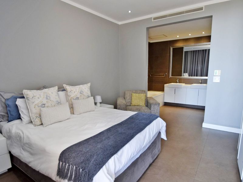 Spacious bedroom featuring an open-plan en-suite bathroom with a double vanity, built-in bathtub, and modern tiled flooring.