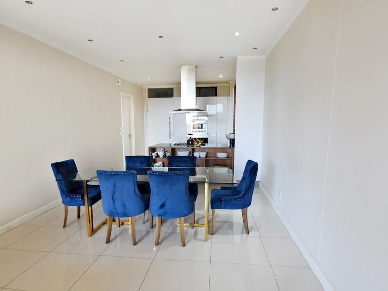 Modern open-plan living and dining area featuring sleek cabinetry, a stainless steel extractor fan, built-in oven, and polished tiled flooring throughout.