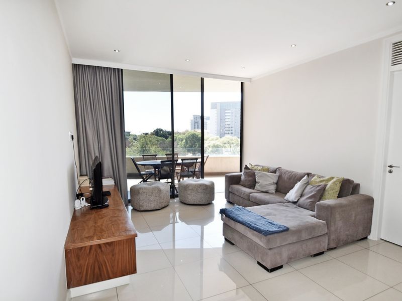 Bright and modern living room featuring large sliding glass doors that open onto a balcony, complemented by sleek tiled flooring and recessed lighting.