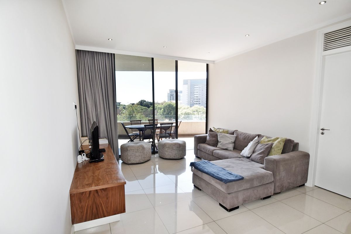 Bright and modern living room featuring large sliding glass doors that open onto a balcony, complemented by sleek tiled flooring and recessed lighting.