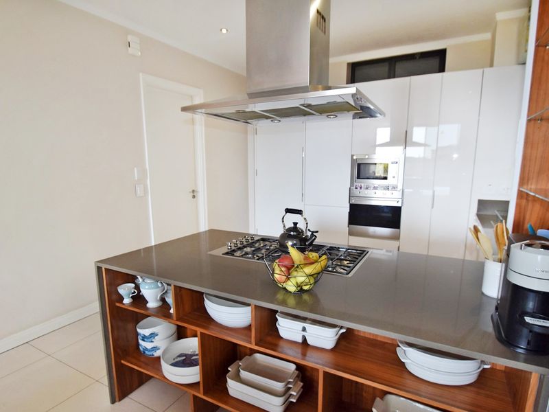 Modern kitchen featuring a central island with a gas hob, stainless steel extractor fan, built-in oven, microwave, and sleek high-gloss cabinetry.