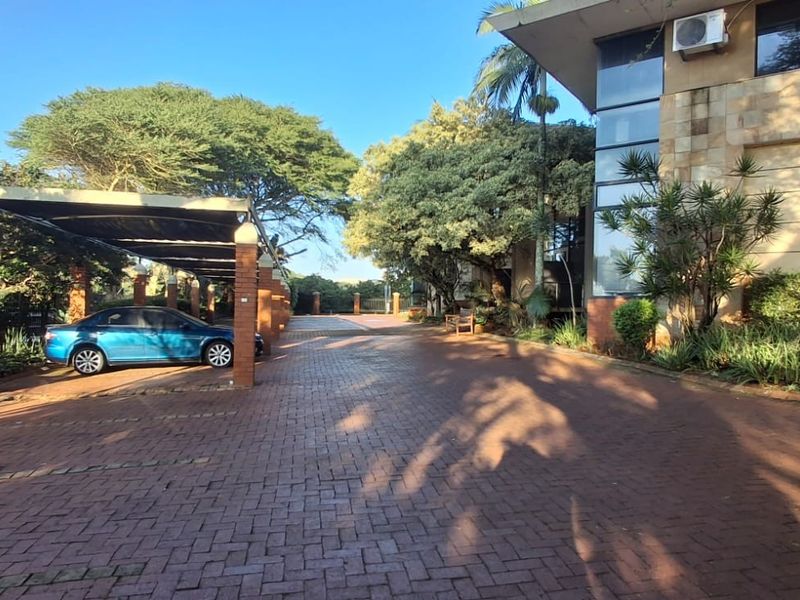 Commercial property exterior featuring a brick paved driveway, covered parking bays, and stone-clad building facade with established landscaping.