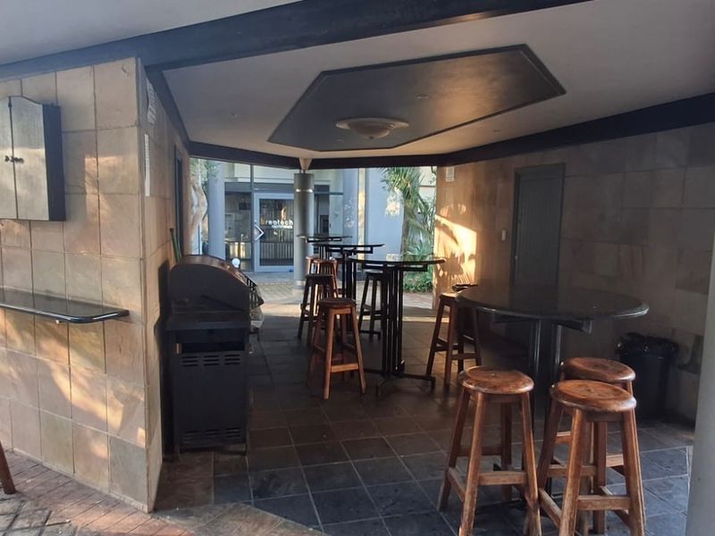 A covered outdoor patio area featuring stone wall cladding, tiled flooring, and a built-in bar counter, suitable for commercial or social gatherings.