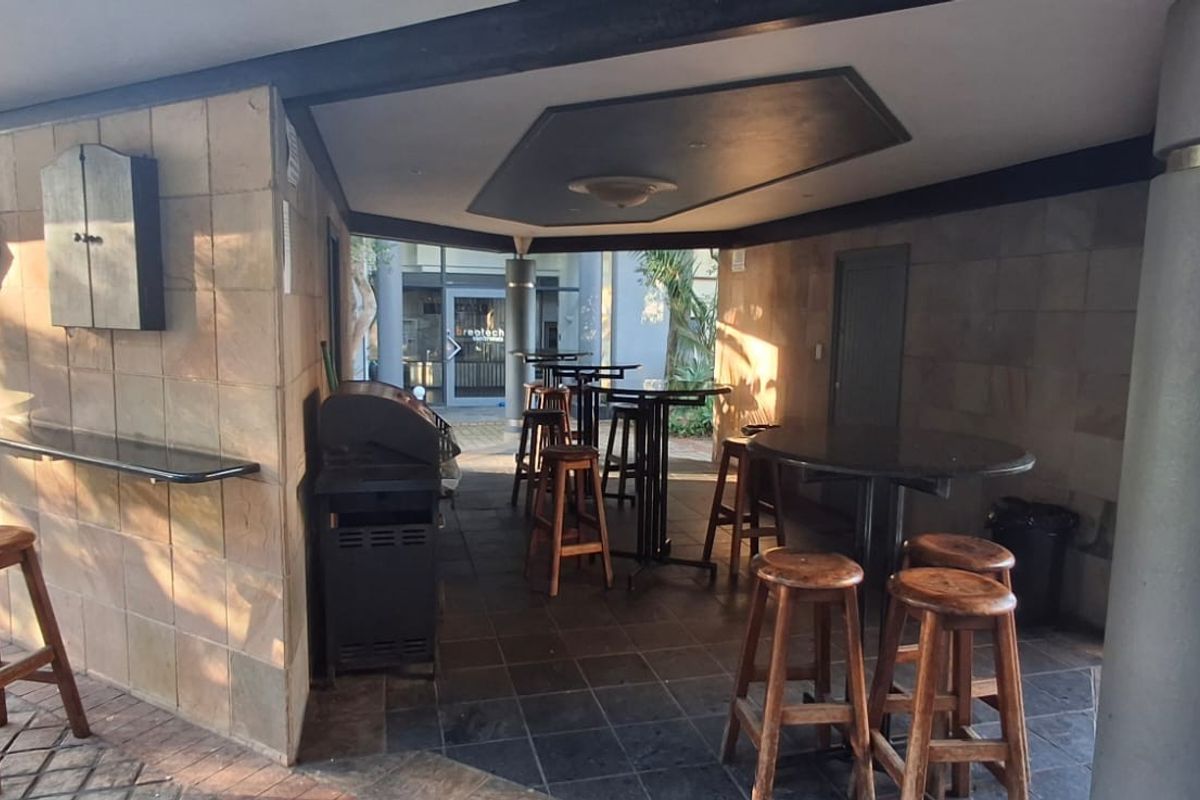 A covered outdoor patio area featuring stone wall cladding, tiled flooring, and a built-in bar counter, suitable for commercial or social gatherings.