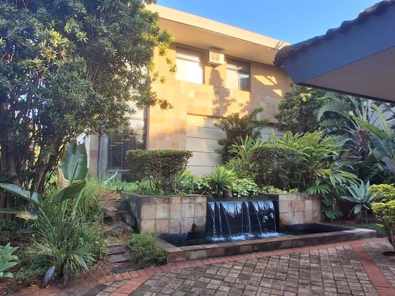 A well-maintained rear exterior area featuring a stone-tiled water feature, paved patio space, and established garden landscaping against the building facade.