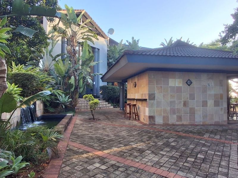 A landscaped rear courtyard featuring a stone-tiled gazebo with a built-in bar counter and a tranquil water feature.
