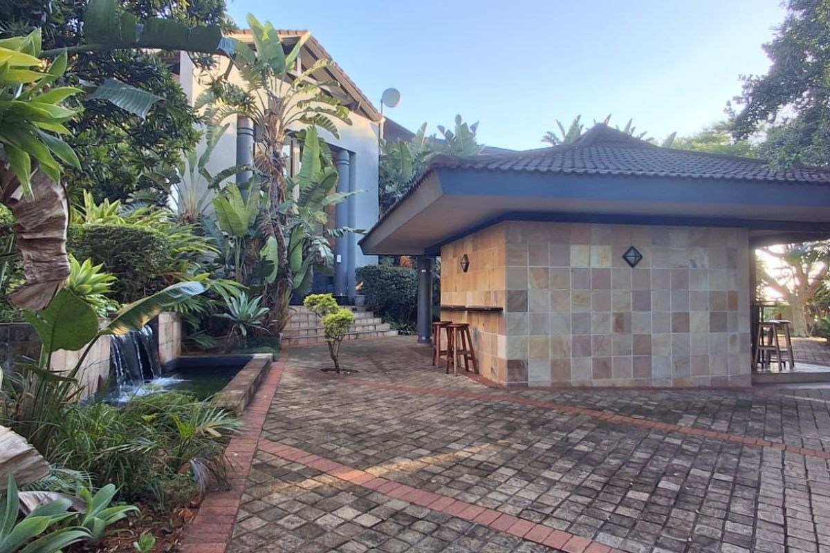 A landscaped rear courtyard featuring a stone-tiled gazebo with a built-in bar counter and a tranquil water feature.
